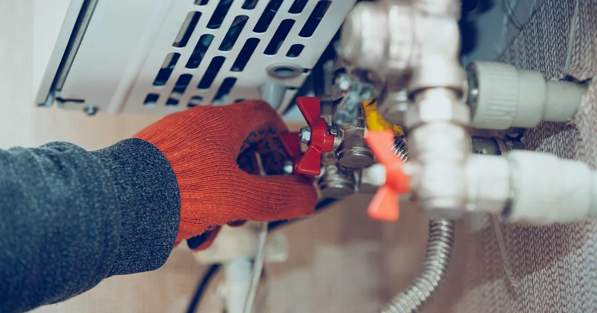 Technician in orange work gloves adjusting valves on a home boiler system